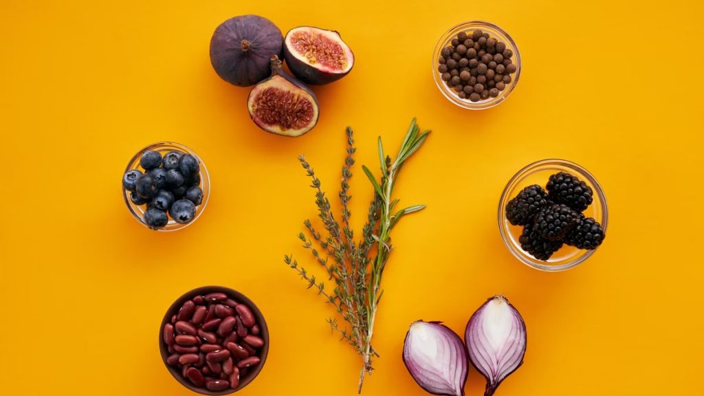 Vibrant flat lay of figs, berries, beans, spices, and herbs on a yellow background.